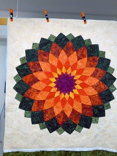 an orange and green flower quilt hanging on a wall