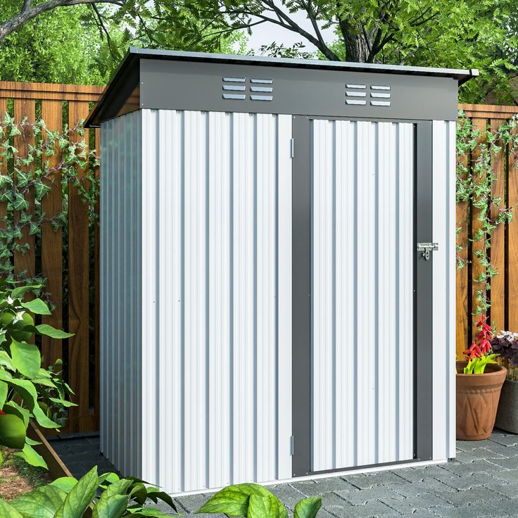 a small white shed sitting in the middle of a yard next to a wooden fence