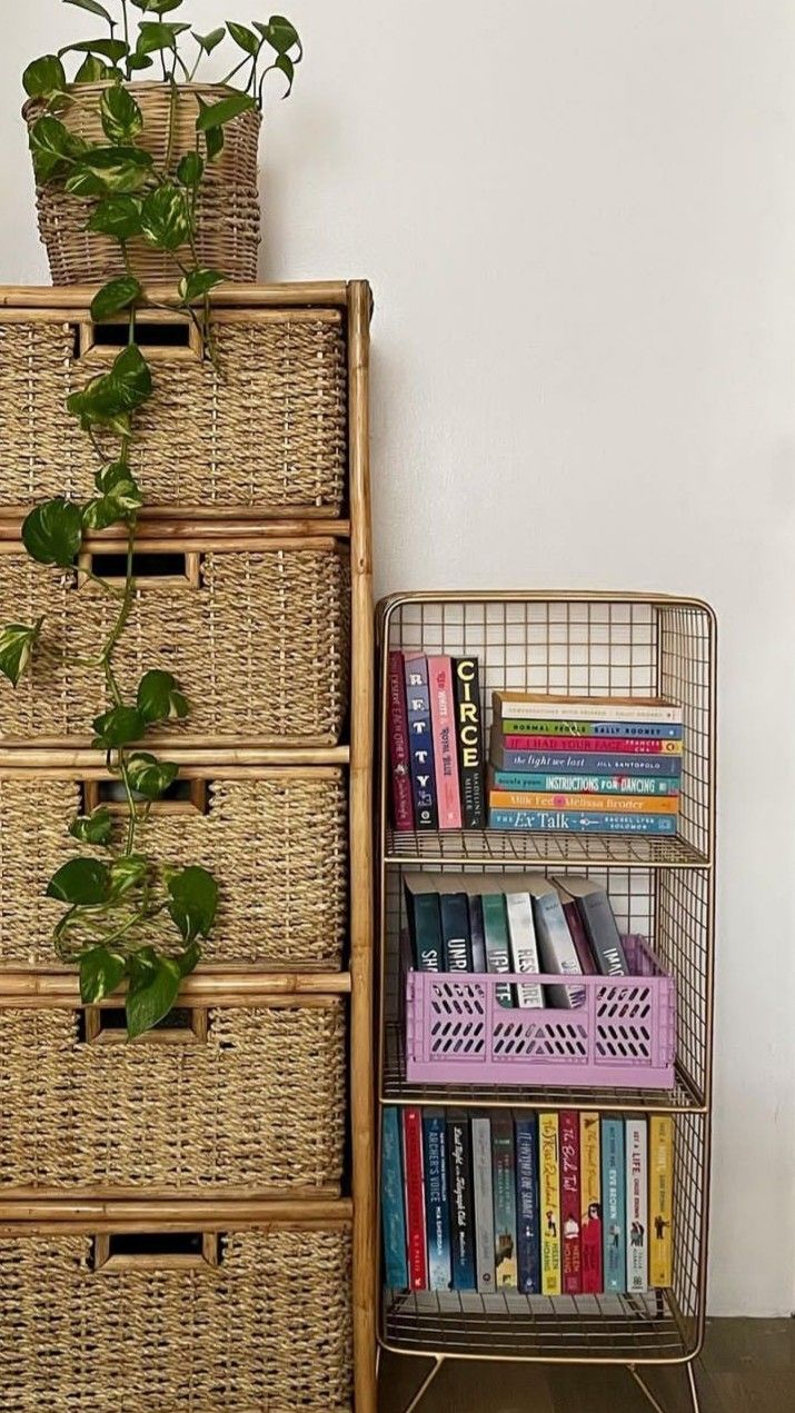 a wicker book shelf with books and plants on it next to a basket filled with books