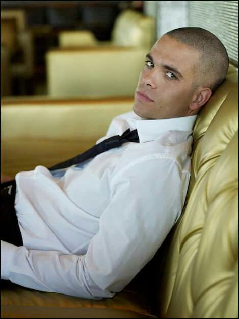 a man in a white shirt and black tie sitting on a yellow leather chair with his legs crossed