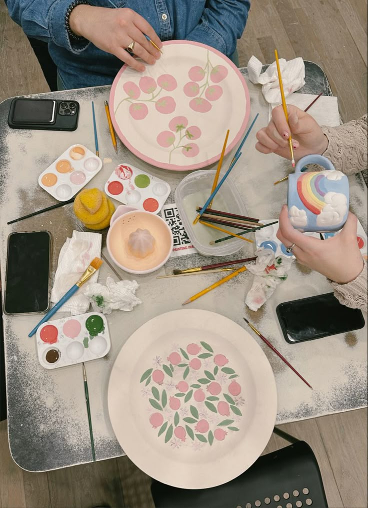 two people sitting at a table with plates and paintbrushes