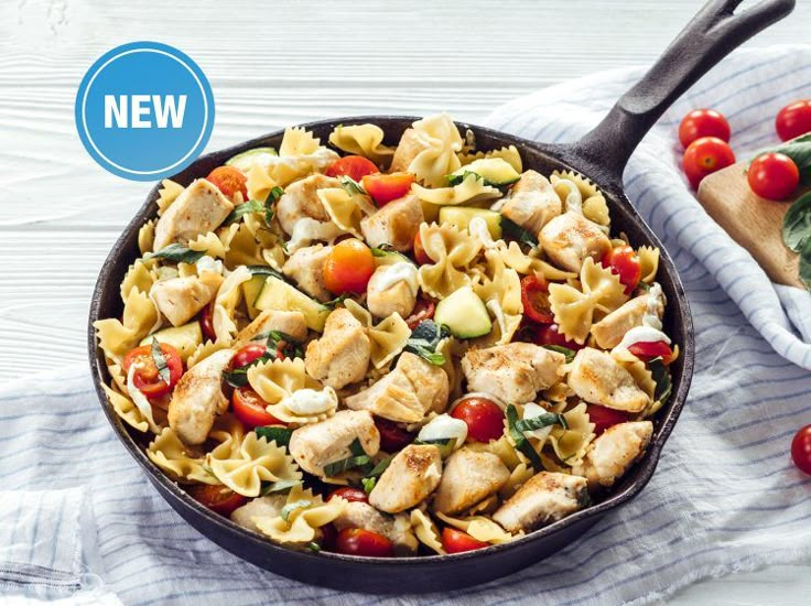 a skillet filled with pasta and chicken next to fresh spinach on a towel