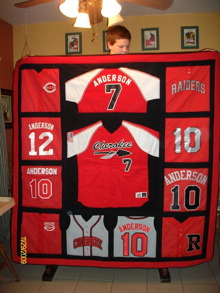 a young boy standing in front of a red and black baseball jersey quilted to the ceiling