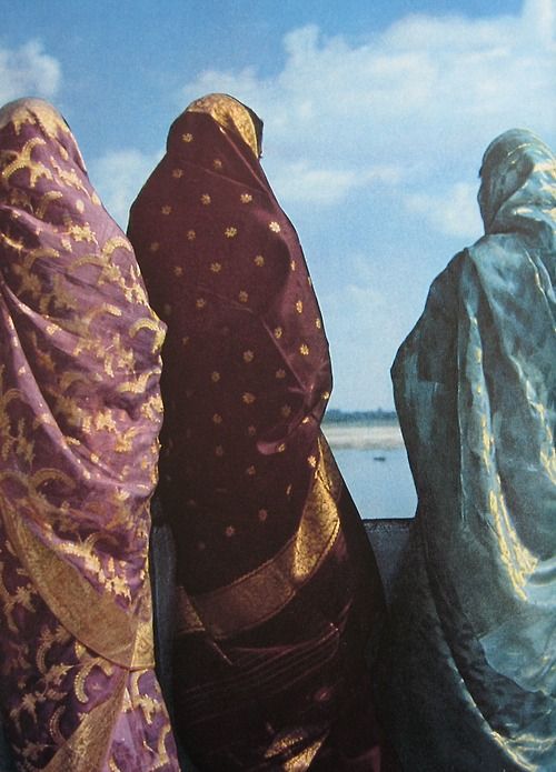 three women sitting on the back of a boat looking out at the water and clouds