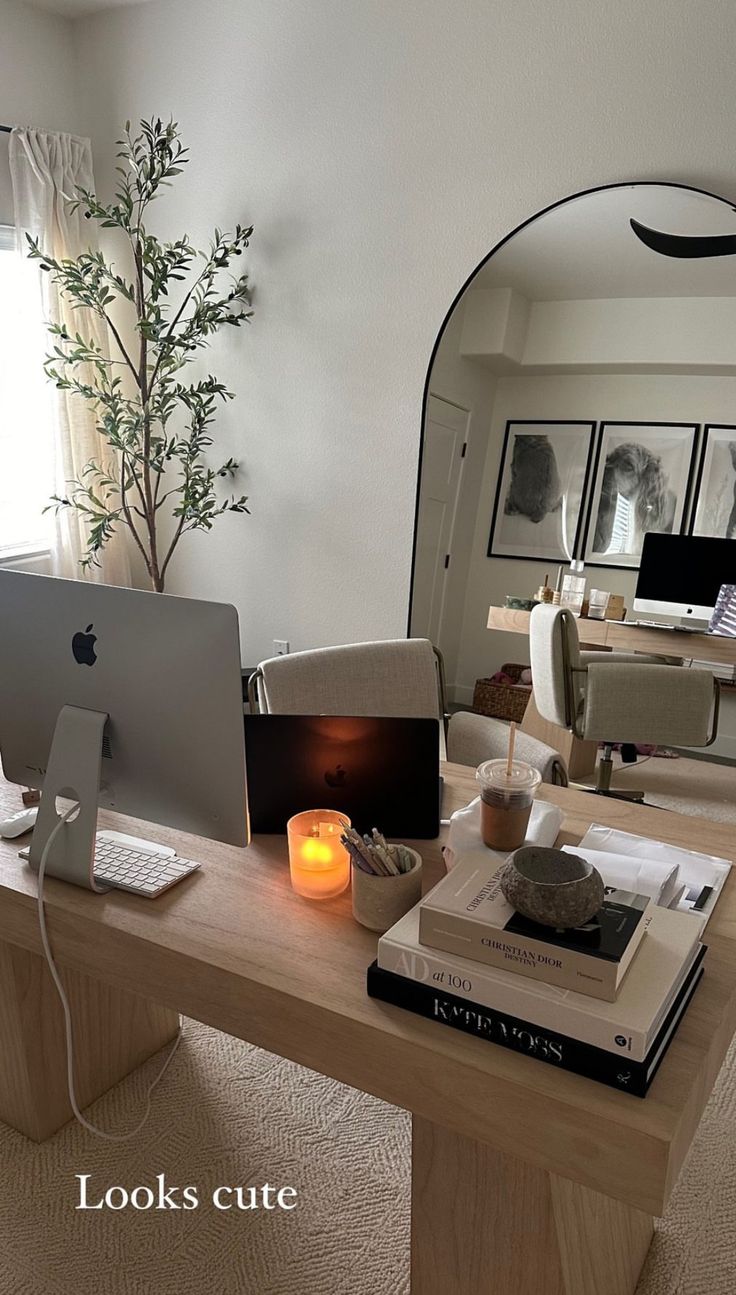 an apple computer sitting on top of a wooden desk in front of a mirror with a lit candle