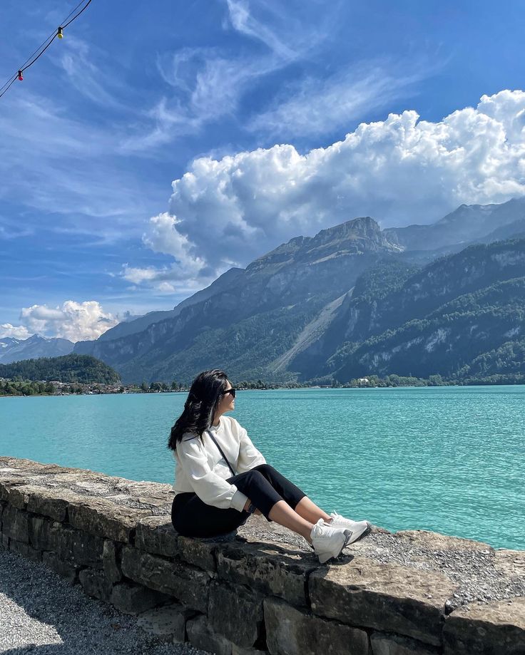 a woman sitting on the edge of a stone wall next to a body of water