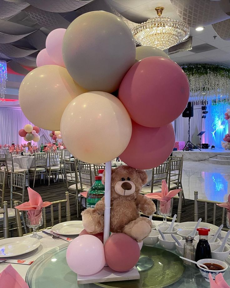 a teddy bear sitting on top of a table with balloons in the shape of flowers