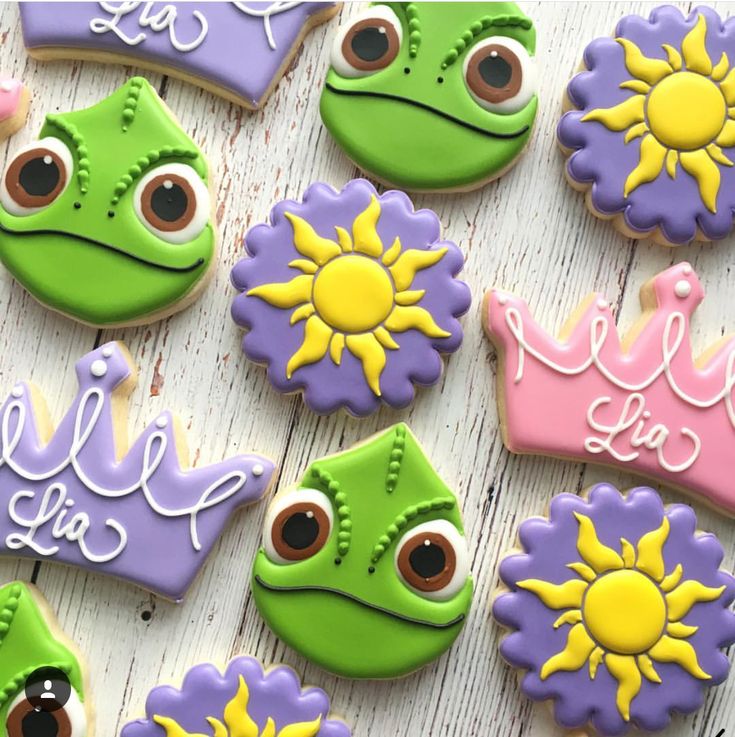 decorated cookies are arranged on a table with princess and frog faces in the middle one cookie has been cut out to look like they's smiling