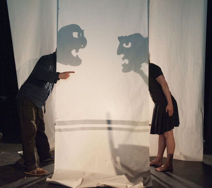 a man and woman standing in front of a white screen with shadows on it, facing each other