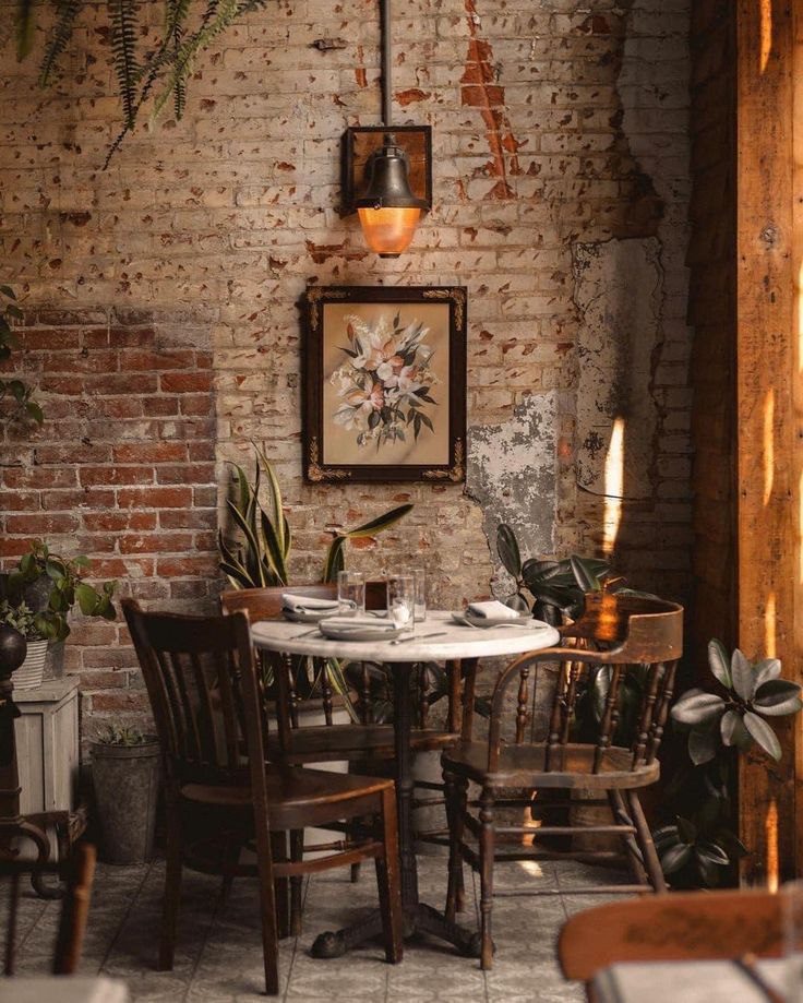 a table and chairs in a room with brick walls, potted plants on the wall