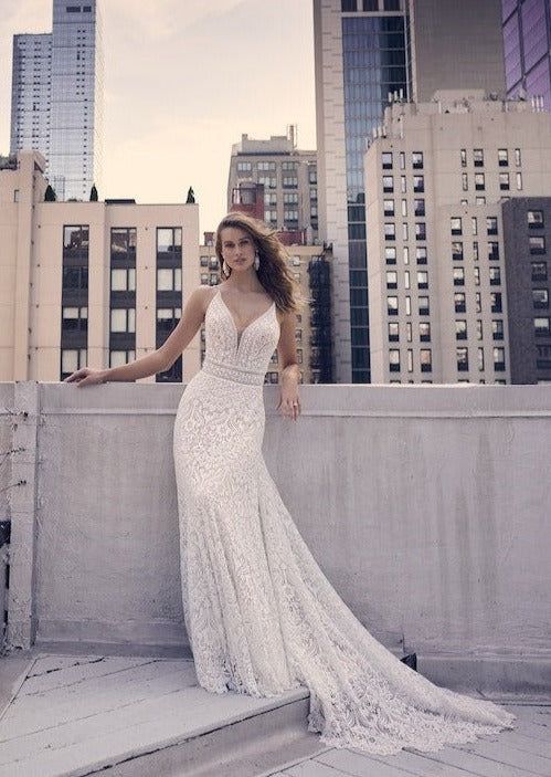 a beautiful woman in a white dress standing on the edge of a building with her arms outstretched