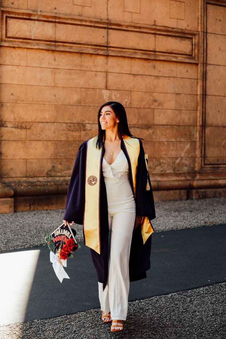 a woman is walking down the street with flowers in her hand and wearing a graduation robe