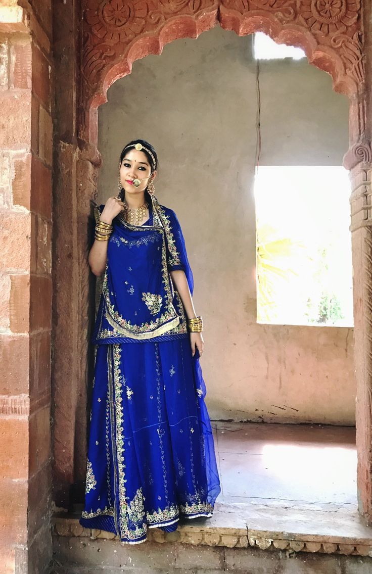 a woman in a blue dress standing by a wall with an arch and window behind her