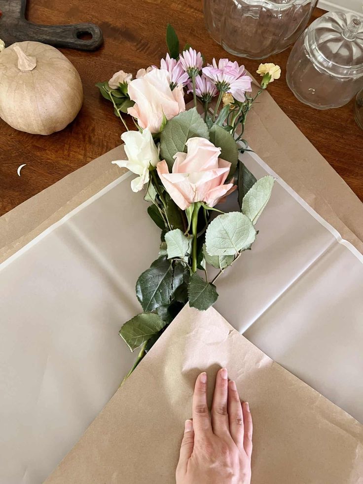 someone is arranging flowers on top of a paper bag and wrapping them in brown paper