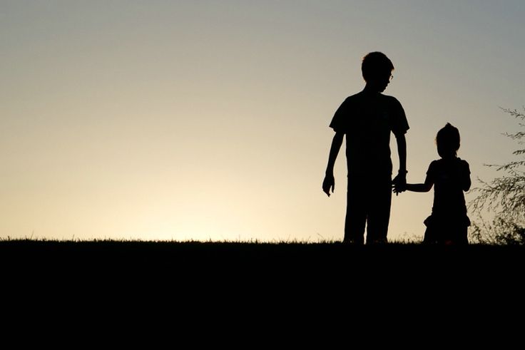 a silhouette of a person holding the hand of a child in front of a sunset