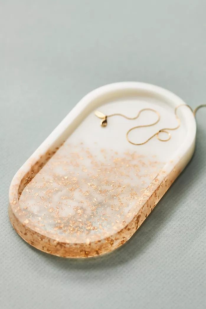 a white and gold tray with some type of jewelry hanging from it's side