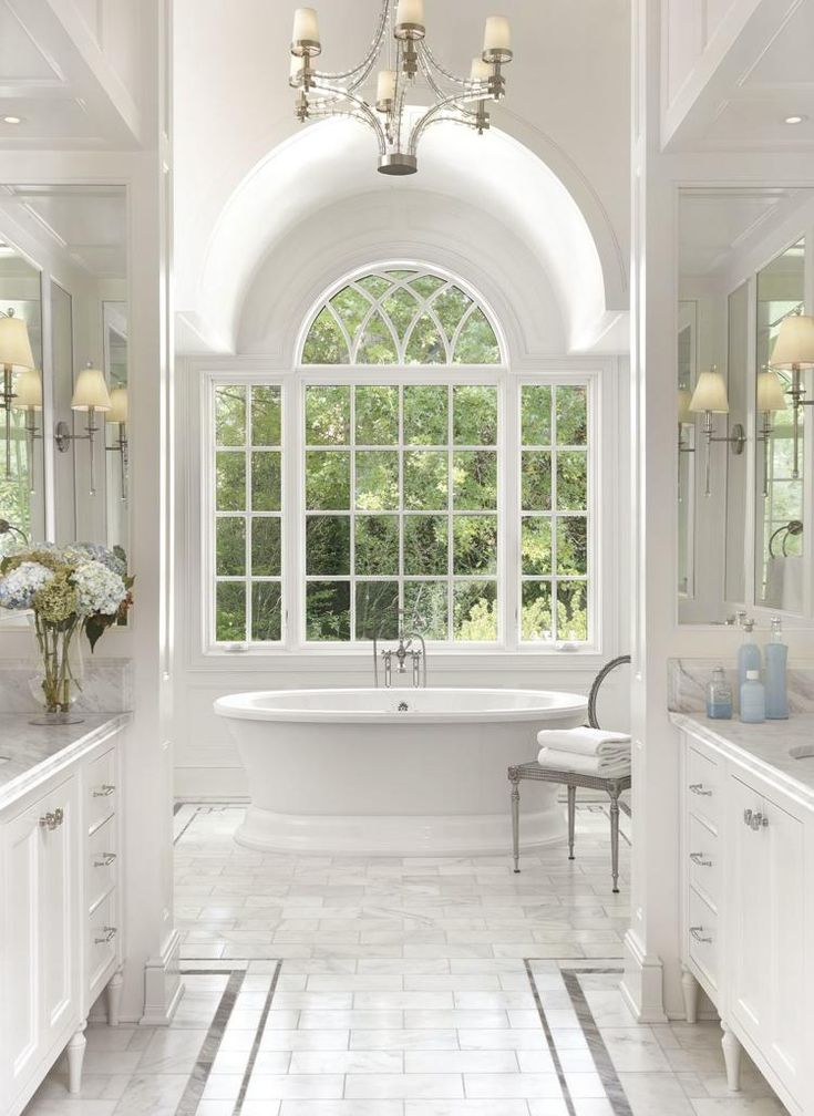 a white bathroom with an arched window and claw foot tub in the center, surrounded by marble tile flooring