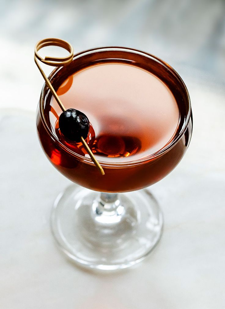 a close up of a drink in a wine glass with a garnish on the rim