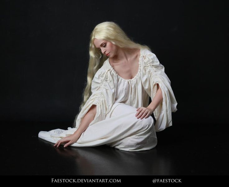 a woman with long blonde hair sitting on the floor in white dress and black background