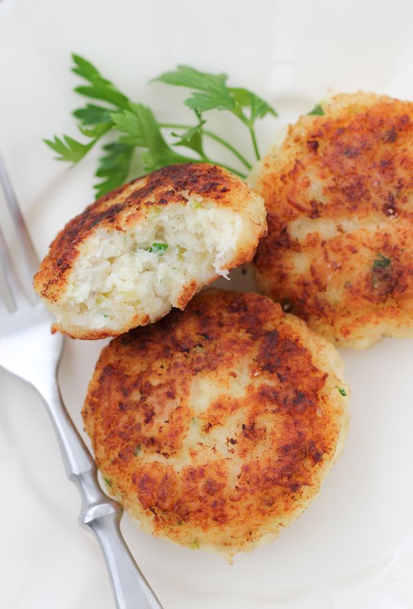 two crab cakes on a white plate with a fork and parsley garnish