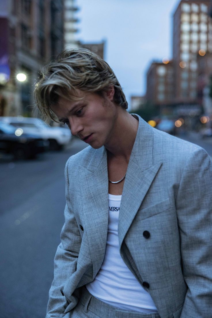 a young man in a suit is standing on the street looking down at his cell phone