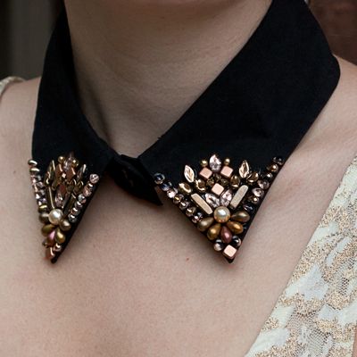 a close up of a woman wearing a black bow tie with gold and pearls on it