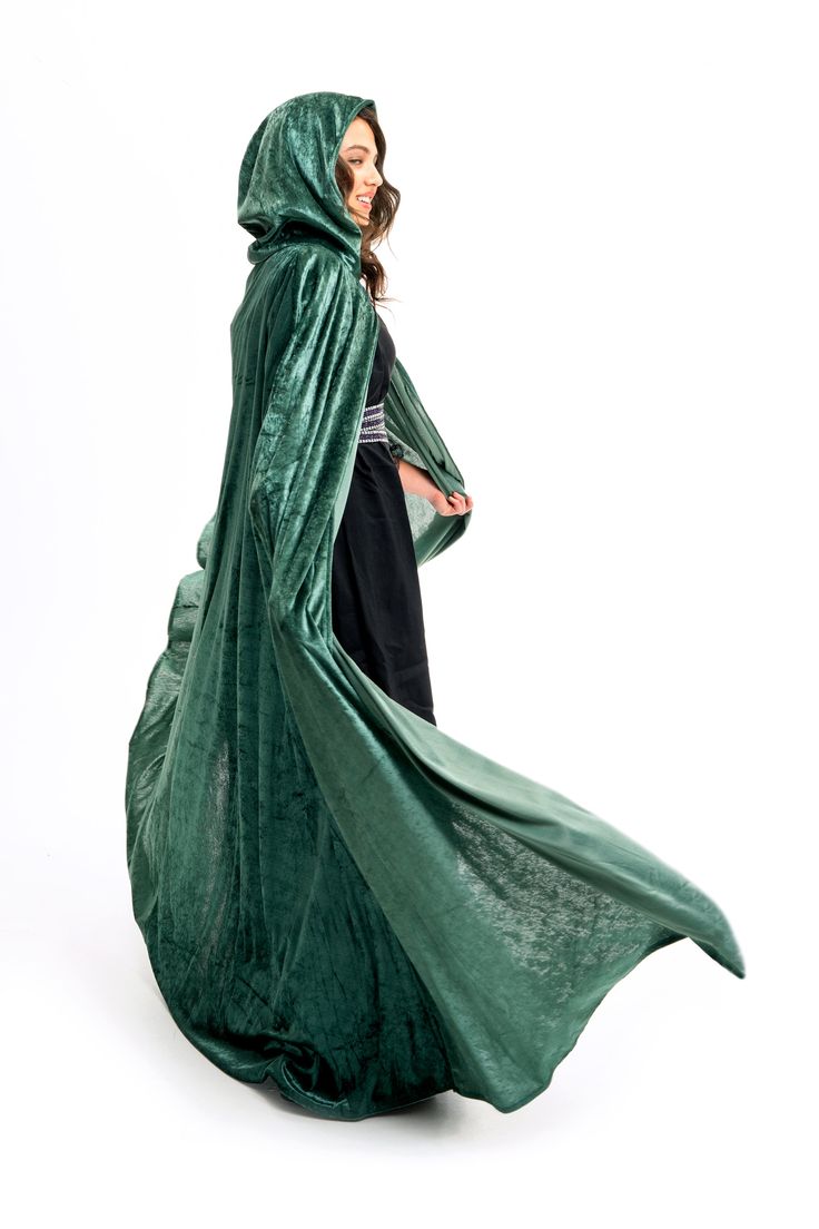 a woman in a green cloak and black dress is standing with her hands on her hips