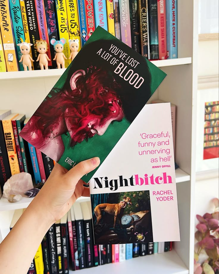 a person holding up a book in front of a bookshelf