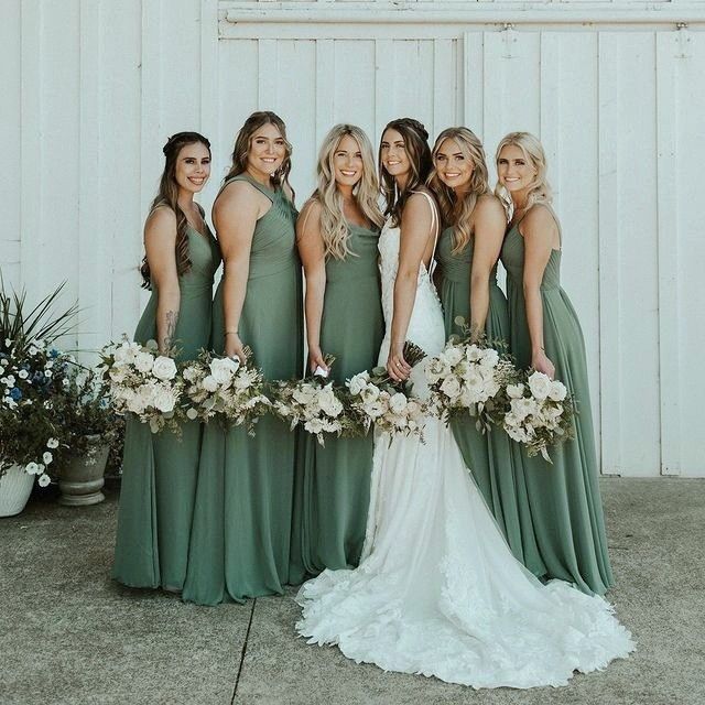 a group of women standing next to each other in front of a white wall holding bouquets