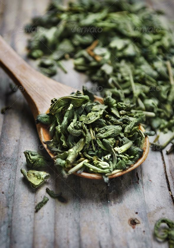 a wooden spoon filled with green tea leaves on top of a wooden table stock photo