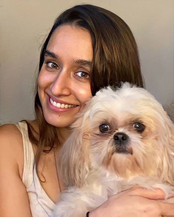 a woman holding a small white dog in her arms and looking at the camera with a smile on her face