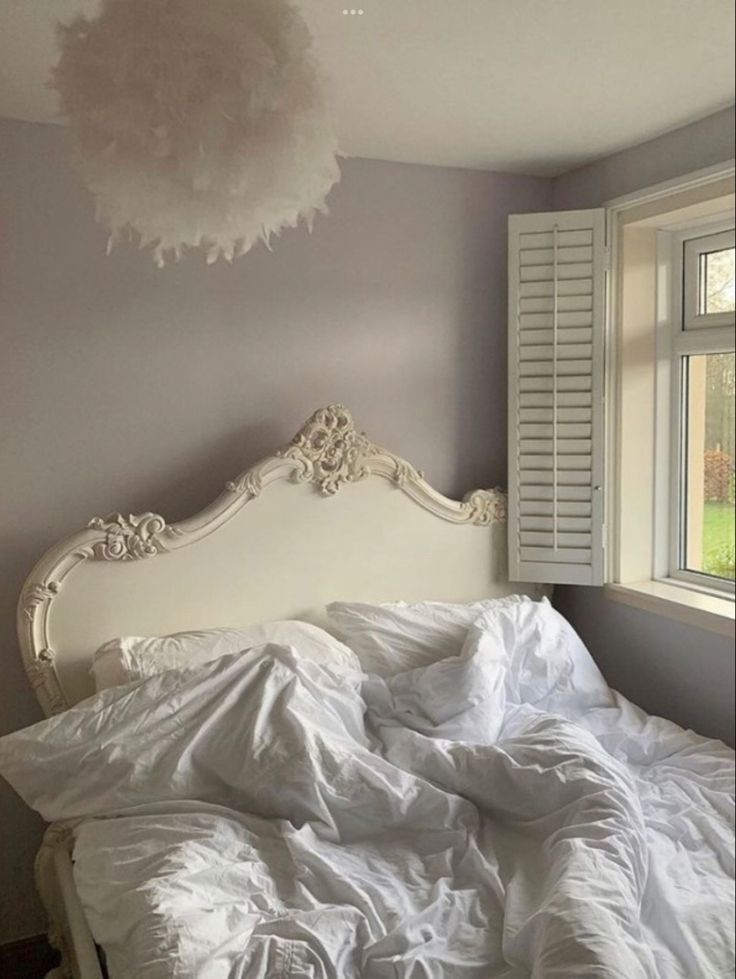 an unmade bed in front of a window with white sheets and pillows on it