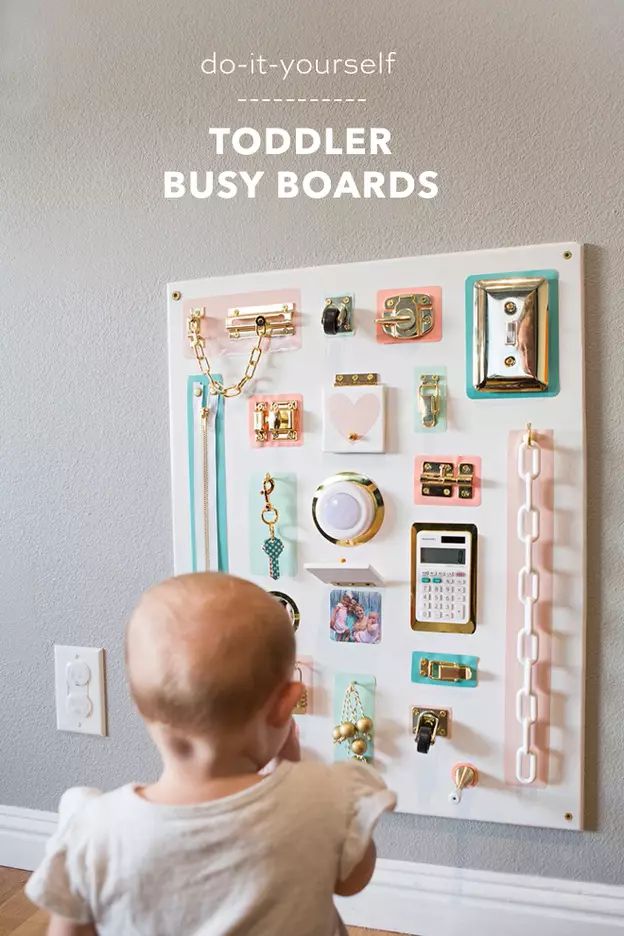 a baby standing in front of a bulletin board with lots of magnets on it