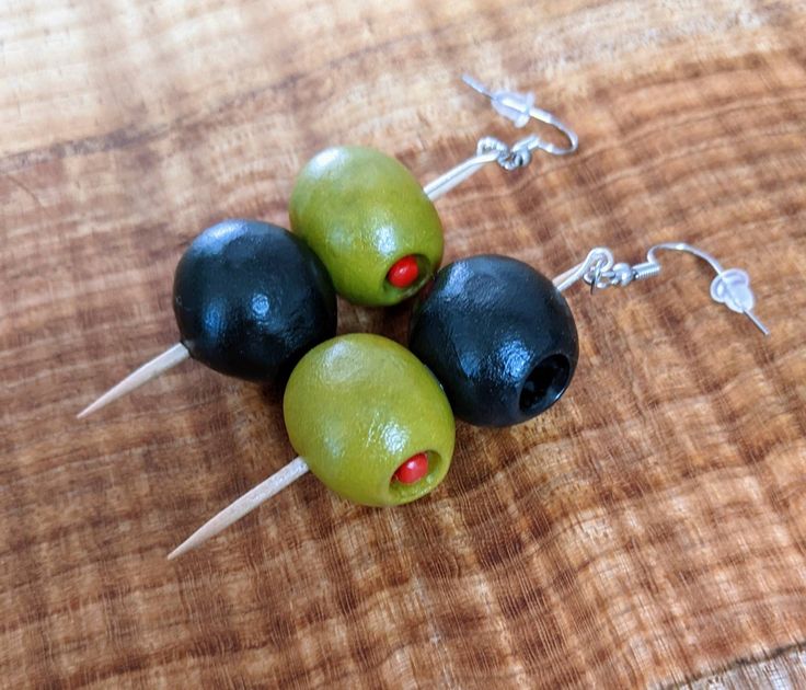 three olives with toothpicks on them sitting on a wooden table next to earrings