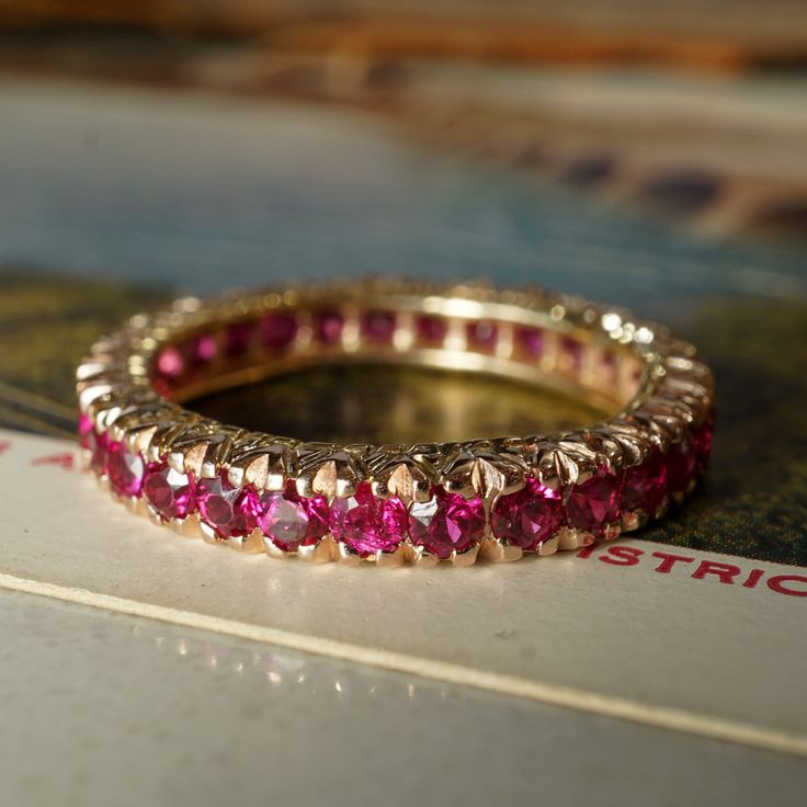 For a special, one of a kind gemstone wedding ring, this modern eternity band features 2.10 carats of round cut rubies in 14 karat yellow gold. Thirty (30) .07 carat rubies with a red-magenta hue are set in shared V prongs around the entire ring. Elegant and practical, this stackable band will bring a depth of color and shine to an engagement ring or can be worn in a right hand stack. Composition: 14k Yellow Gold Era: Modern 1970 - Present Primary Stone: Natural Ruby Shape and Measurements: 2.25 Luxury Ruby Ring For Wedding With Half Eternity Band, Luxury Half Eternity Ruby Ring, Hand Stack, Modern Eternity Band, Gemstone Wedding Ring, Gemstone Wedding, Gemstone Wedding Rings, Ring Elegant, Stackable Bands