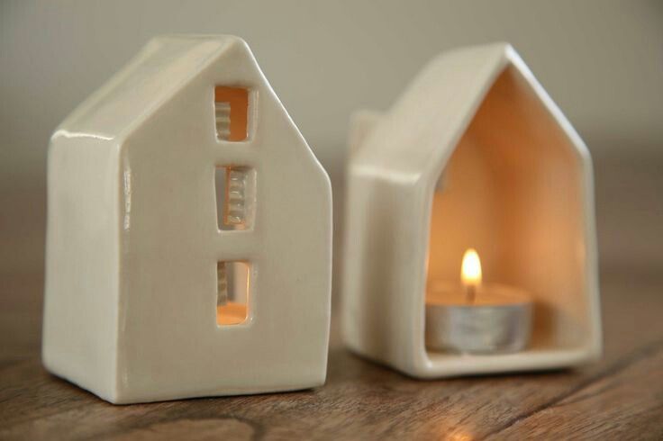 a small white house shaped candle holder with a lit candle in the front and side