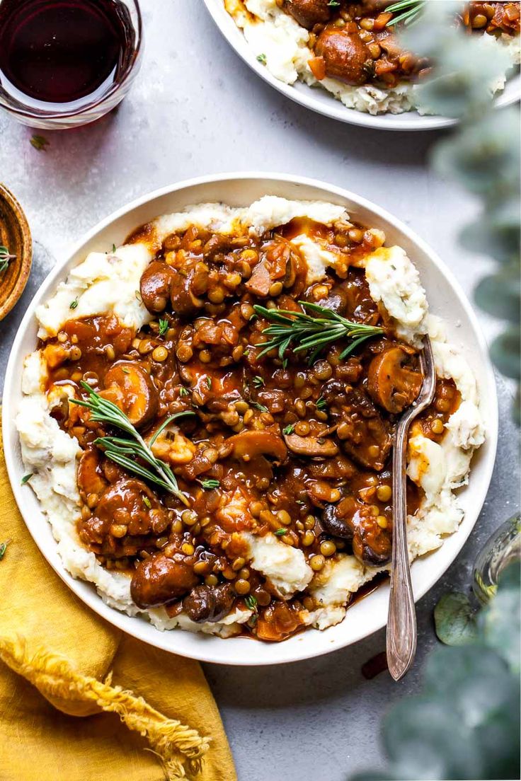 two plates filled with meat and potatoes covered in gravy next to a glass of wine