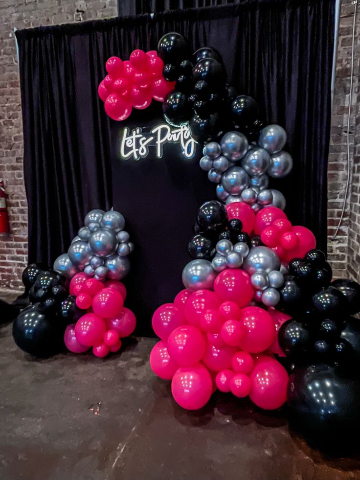 black and silver balloons are arranged in the shape of an arch with flowers on it