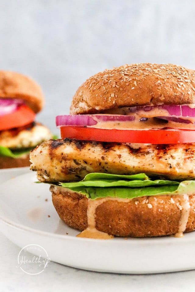 a chicken sandwich with lettuce, tomato and onion on a white platter