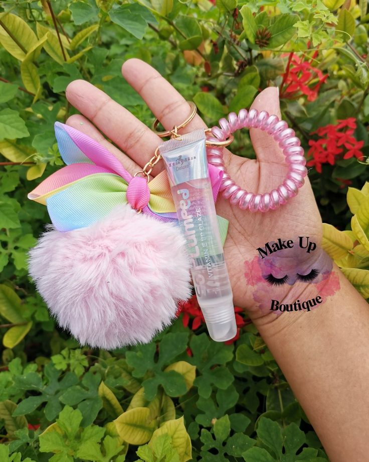 a hand holding a pink and white pom - pom keychain with a small tube of makeup on it