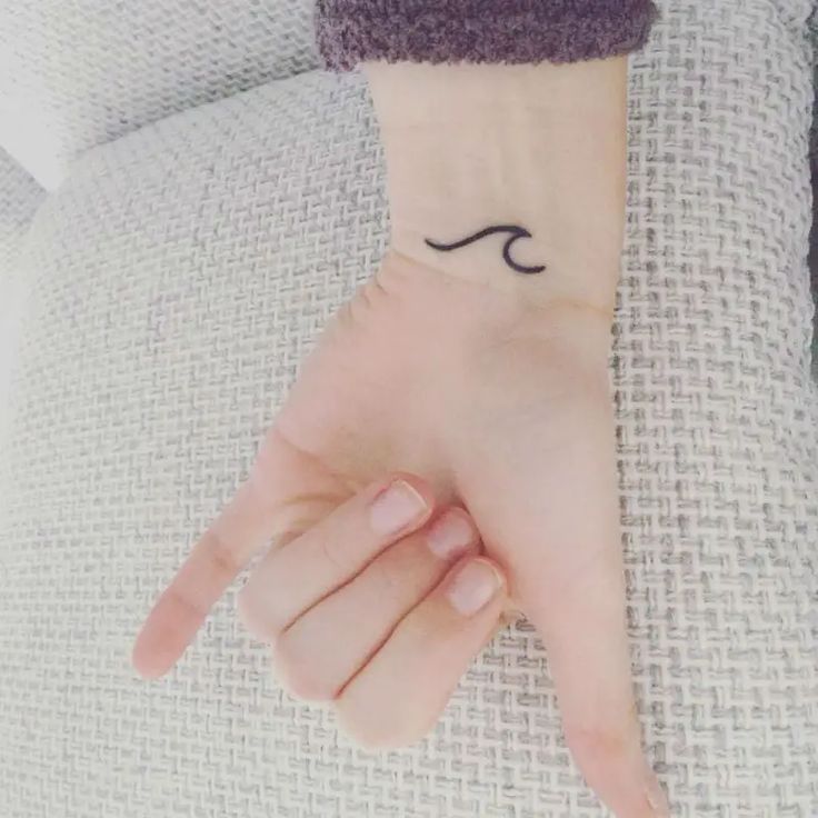 a woman's hand with a small wave tattoo on it