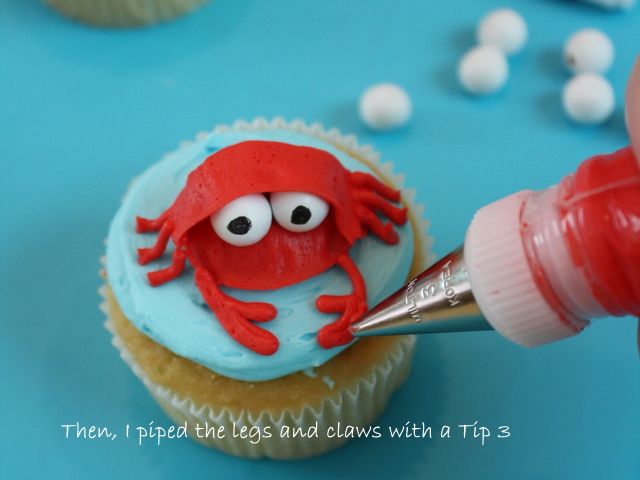 a cupcake with blue icing and a red crab on it being piped into the frosting