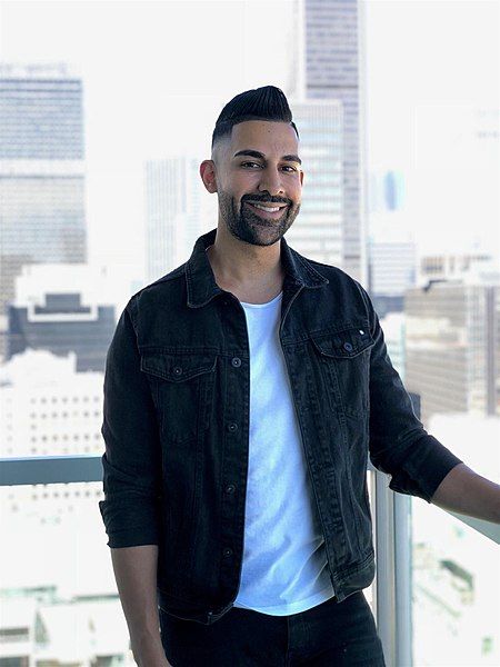 a man standing in front of a window next to a tall building and smiling at the camera