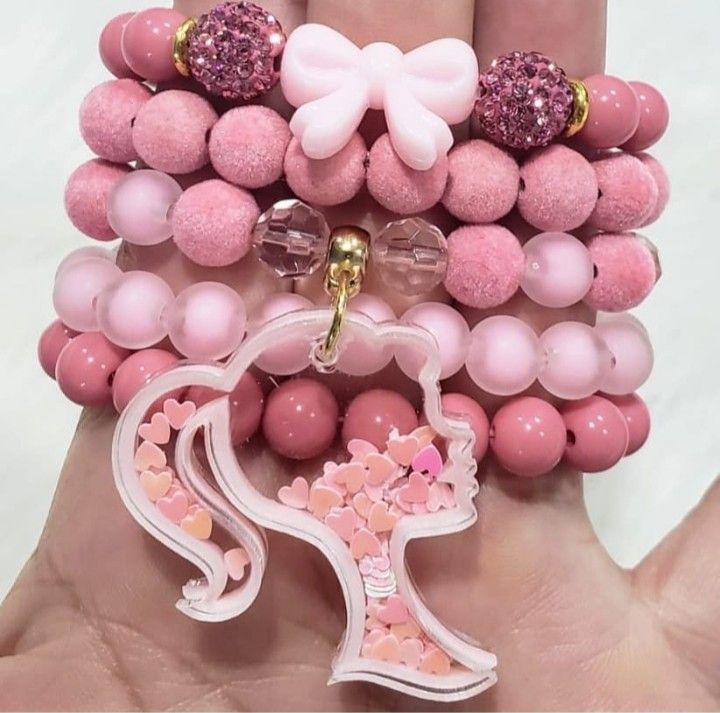 a hand holding several bracelets with pink beads and bows on them, one is wearing a bow