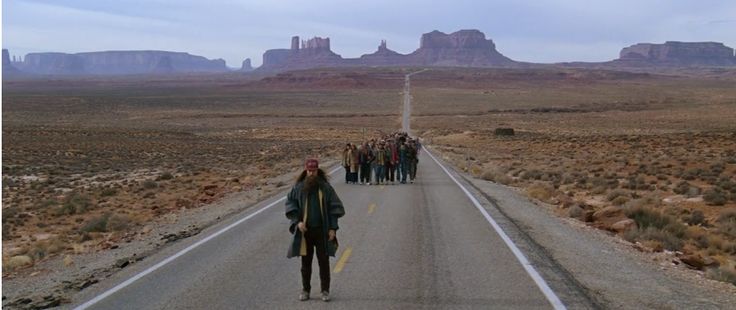 a group of people walking down the middle of an empty road with mountains in the background