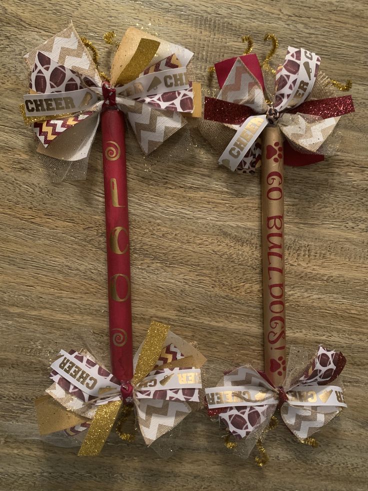 two red and gold pencils with bows on them sitting on a wooden table next to each other