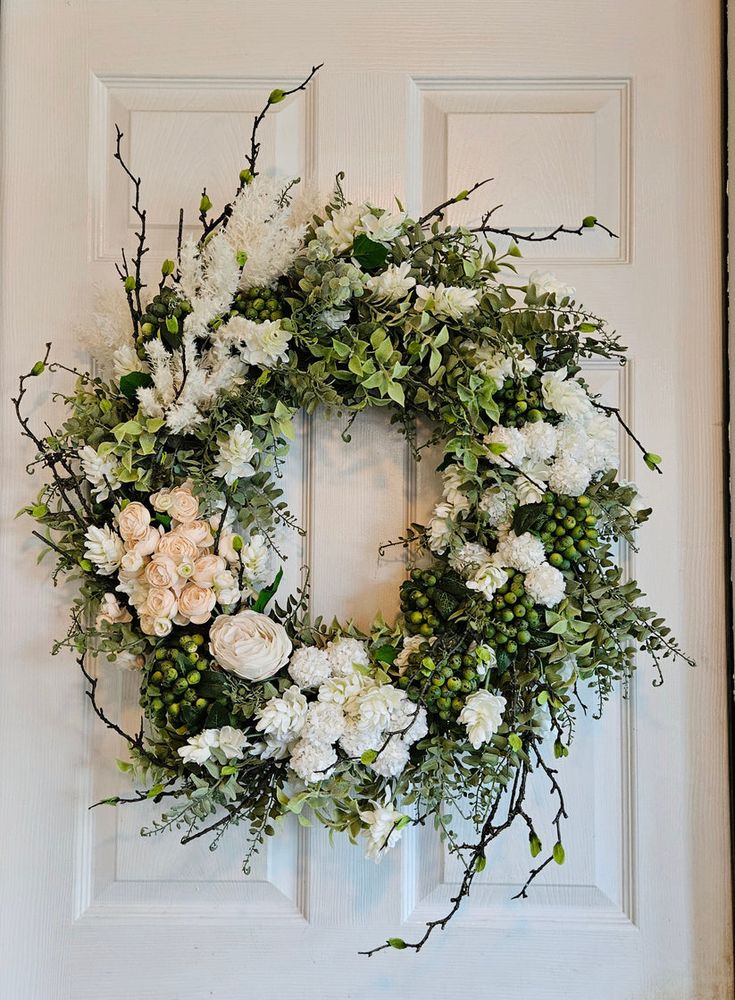 a wreath with white flowers and greenery hangs on the front door