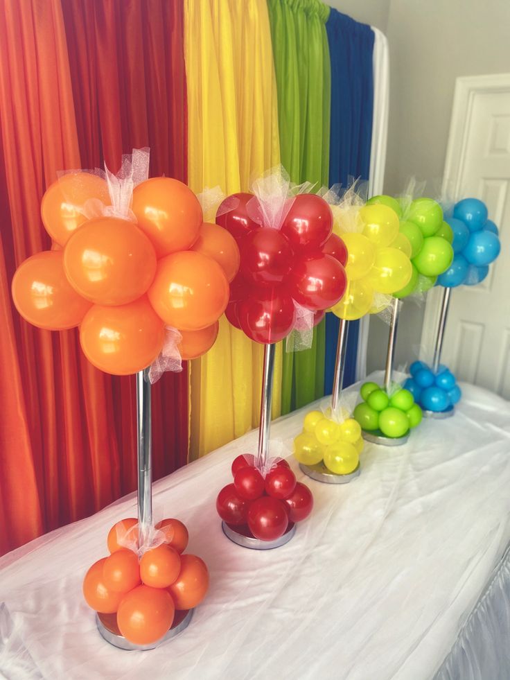 there are many balloons on the table and in front of it is a rainbow curtain