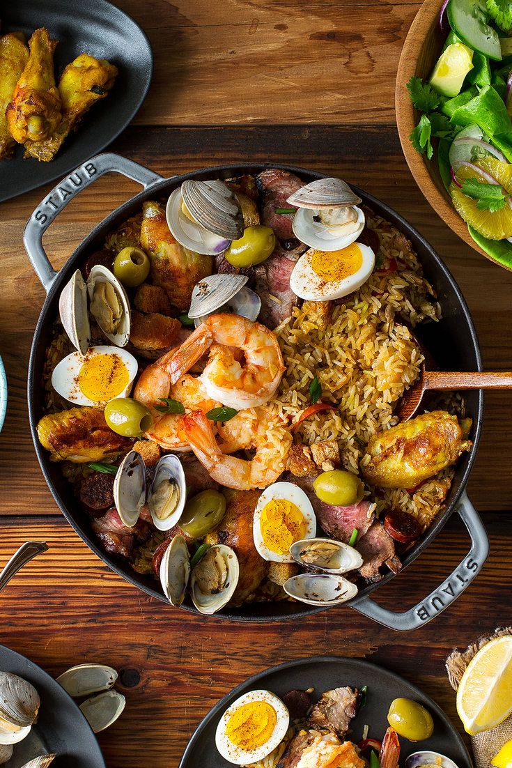 an overhead view of seafood and rice in a skillet on a wooden table with other dishes