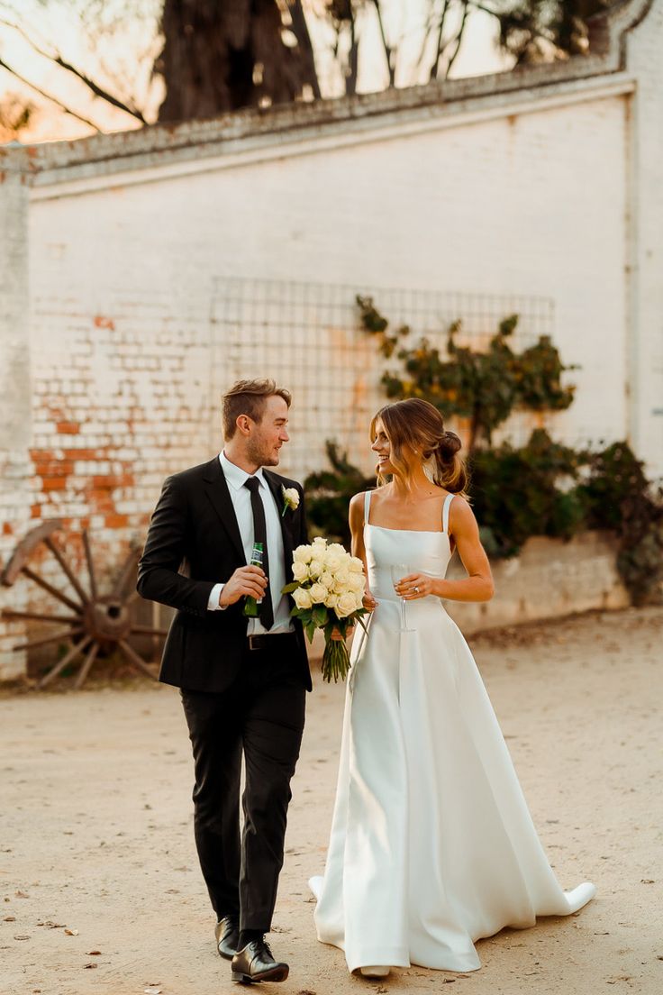 a bride and groom walking down the street together in front of a white building with brick walls